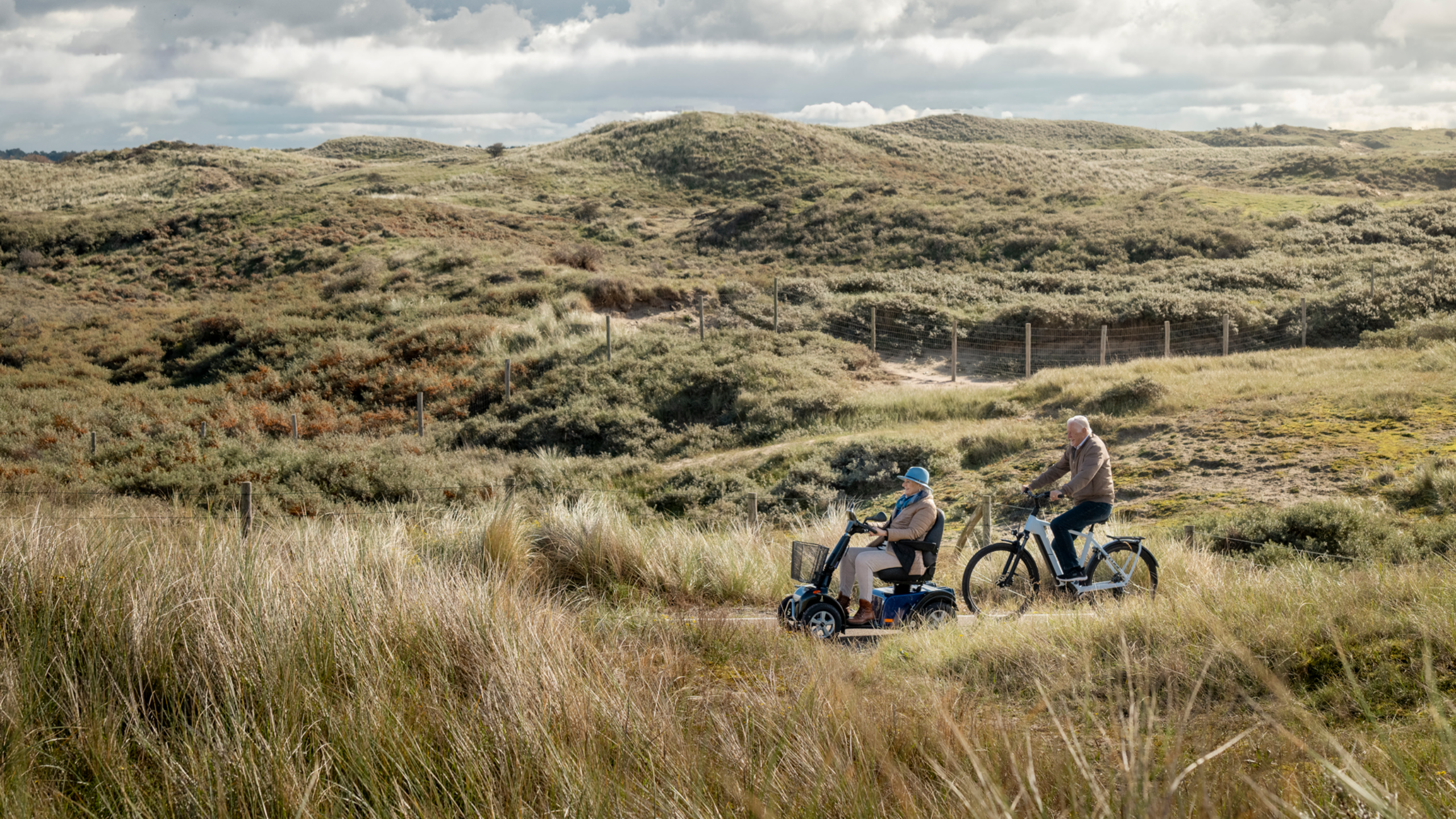 Solo RX 4-wiel scootmobiel rijdt door de duinen naast een fietser